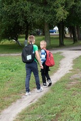 Obraz premium Two young students with backpacks walk along a dirt path on their way home from school through a wooded area. They are friendly.
