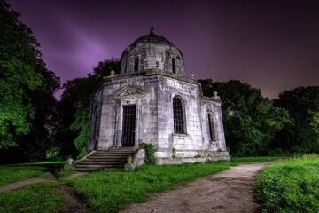 Fototapeta premium Aged stone gazebo at night, surrounded by trees and a path