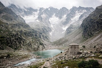 Alpine lake nestled in a rocky valley, with a stone hut and snow-capped peaks in the background