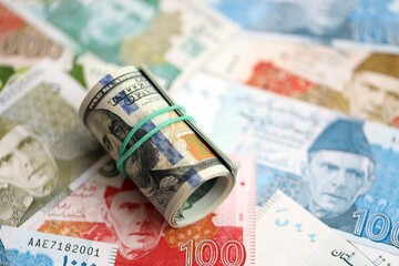 Roll of US dollar bills lies on big amount of Pakistan rupees banknotes close up