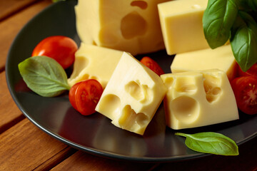 Swiss cheese, green basil, salad, and tomatoes on a wooden table.