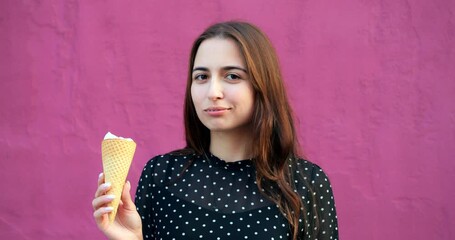 Young woman looking at ice cream cone with contemplative gaze by vibrant pink wall, cone melting softly, concept cinematic shot framing cone detail and wall contrast for casual treat vibe.