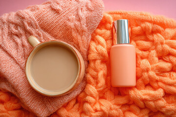 Cozy flat lay with orange knitted sweater, warm coffee cup, and peach cosmetic bottle on soft textured background, creating relaxing and aesthetic morning vibe