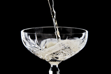 Golden champagne or sparkling wine pouring into an elegant crystal coupe glass, creating a foamy head against a dramatic black background, perfect for celebrations and luxury.