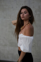 Naklejka premium Stylish young woman in fashionable clothes posing confidently outdoors. Fashion model look with urban background, long hair, black shoes, and modern accessories.