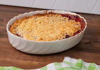 traditional plum crumble pie in white ceramic dish on wooden kitchen counter. rustic fruit dessert with golden crust and juicy filling. concept of homemade baking, seasonal treats, culinary blog