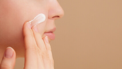 Close-up half face portrait unrecognizable woman applying moisturising cream, sunscreen, makeup preparation. Beauty routine ads. Skincare commercial. Self care. Studio shot. Beauty spa. Copy space