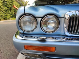 Close-up of a classic car's dual round headlights and chrome grille, showcasing its vintage design and blue body parked by the roadside.