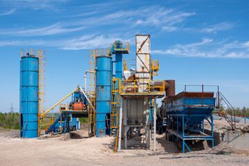 Industrial asphalt mixing plant with blue silos and conveyors under clear sky. concept of heavy...
