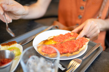 Woman eating pa amb tomàquet in a restaurant with glass of water and sauces