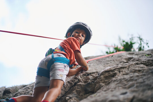 Smiling boy climbing natural rock wall with helmet and safety harness