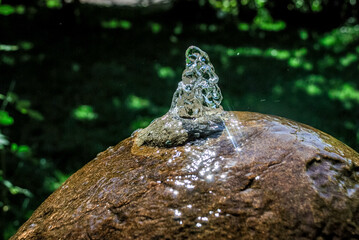 Sunlit water fountain splashing on stone ball in lush outdoor garden