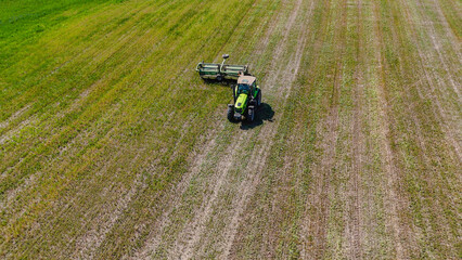 a green tractor with a mower is mowing medicinal herbs in a field