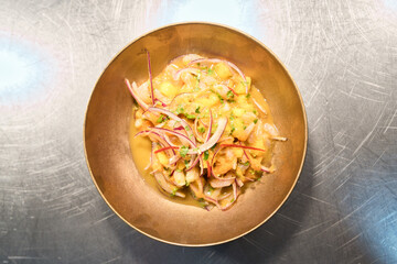 Overhead view of vibrant ceviche featuring fresh shrimp, citrus marinated mango, red onion, and cilantro, elegantly presented in a golden bowl on stainless steel