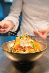 Professional chef garnishing vibrant ceviche with crispy plantain chips and microgreens in an elegant brass bowl, highlighting culinary expertise and artistic presentation