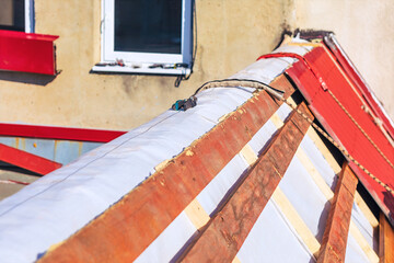 Roof repair in progress with exposed wooden battens and protective underlayment covering attic structure. Old tiles have been partially removed, revealing renovation work beneath