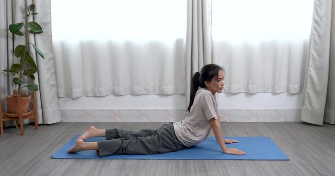 asian woman lying on mat pressing palms into floor while arching back upward in cobra yoga pose during morning indoor session to strengthen spine and promote body awareness and energy