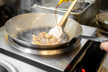 Professional chef stir-frying vegetables and meat in a wok, pouring sauce over steaming ingredients in a vibrant kitchen setting.