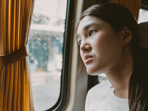 Asian female looking out train window in daylight - Powered by Adobe