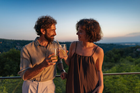 Couple enjoying drinks on balcony at sunset with panoramic view - Powered by Adobe