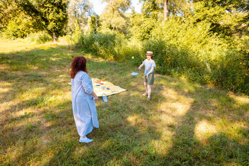 Fototapeta premium Caucasian woman and her daughter enjoy badminton in a green park with trees. Real people, outdoor game, bonding and holiday mood.