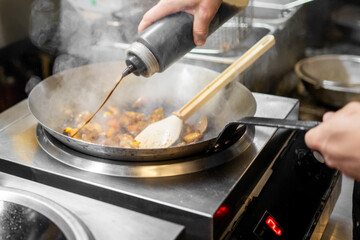 Chef pouring sauce into sizzling stir-fry in hot pan, steam rising as ingredients are mixed on stove in dynamic kitchen cooking scene