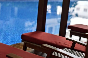 Serene Poolside Loungers Red Cushions Wooden Frames and Tranquil Blue Water.