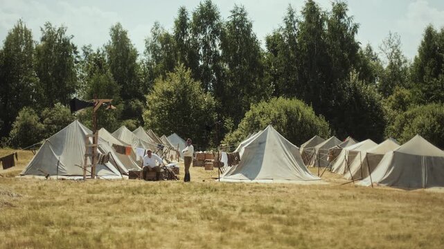 Soviet Army field camp of Red Army soldiers, two infantrymen without uniforms sit near white tents. Great Patriotic War re-enactment. Second world War performance. Wide long shot. Summer 1944 in USSR