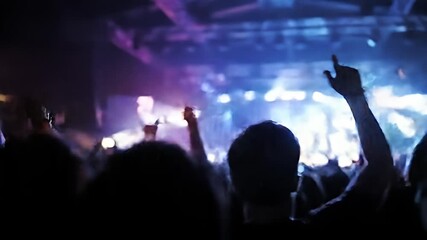 Audience views stage with performer in bright spotlight, crowd raises hands