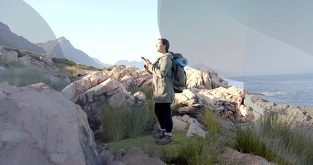 Woman hiker tapping smartphone showing AR shapes, pinching and swiping before scanning horizon - Powered by Adobe