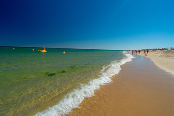 Obraz premium Relaxed summer holiday atmosphere with crystal clear sea waters and a yellow leisure boat with a red slide floating in the calm waters of Barril beach - Santa Luzia - Tavira - Algarve - Portugal