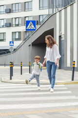 Mother and playful son crossing street together. Back to school