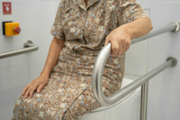 Asian elderly woman patient use toilet support rail in bathroom.