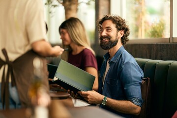 Smiling Man Holding Menu at Restaurant While Interacting With Waitstaff