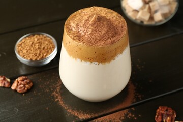 Delicious dalgona coffee in glass, granules, walnuts and brown sugar on wooden table, closeup
