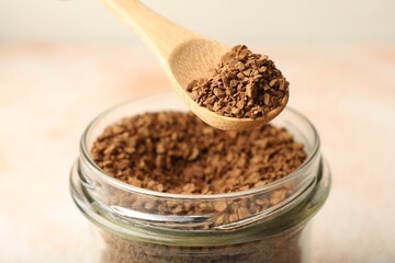 Taking granulated instant coffee from jar with spoon on blurred light background, closeup