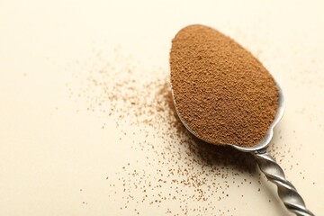 Spoon with instant coffee powder on beige background, closeup. Space for text