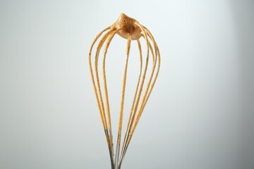 Making delicious dalgona coffee. Whisk with cream on light grey background, closeup