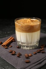 Delicious dalgona coffee in glass, beans and cinnamon on dark table, closeup