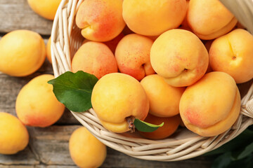 Fresh apricots in wicker basket on wooden table, flat lay