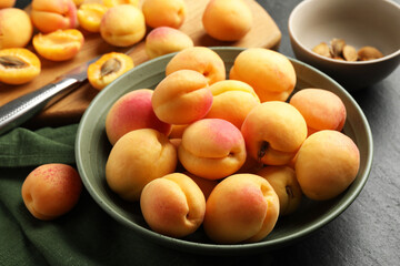 Fresh ripe apricots in bowl, kernels and knife on black table, closeup