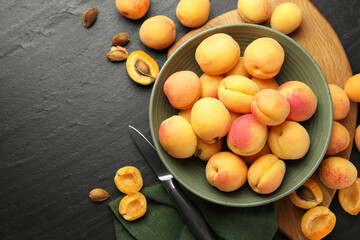 Fresh ripe apricots in bowl and knife on black table, flat lay. Space for text