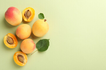 Fresh ripe apricots and leaves on pale green background, flat lay. Space for text