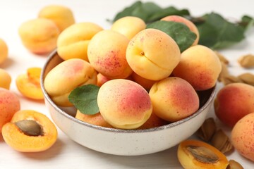 Fresh ripe apricots in bowl and green leaves on white table, closeup