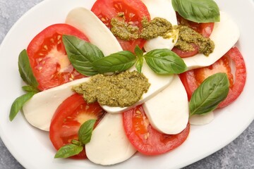 Tasty salad Caprese with mozzarella, tomatoes, basil and pesto sauce on grey table, top view
