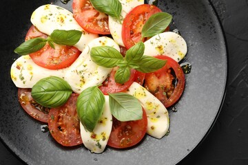 Tasty salad Caprese with mozzarella, tomatoes, basil and spices on black table, top view