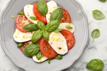 Tasty salad Caprese with mozzarella, tomatoes, basil and spices on white marble table, flat lay
