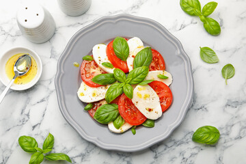 Tasty salad Caprese with mozzarella, tomatoes, basil and spices on white marble table, flat lay