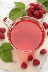 Aromatic raspberry tea in glass cup, berries and green leaves on white marble table, top view