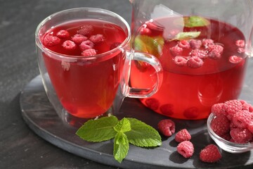Aromatic raspberry tea in glass cup, teapot, berries and mint on black table, closeup